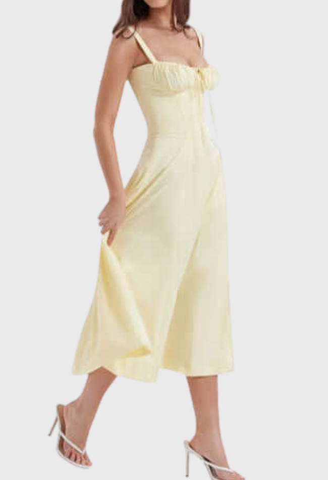 Abito midi giallo chiaro con spalline sottili, scollo a cuore e gonna svasata. Modella indossa sandali bianchi con tacco. Moda estiva elegante.