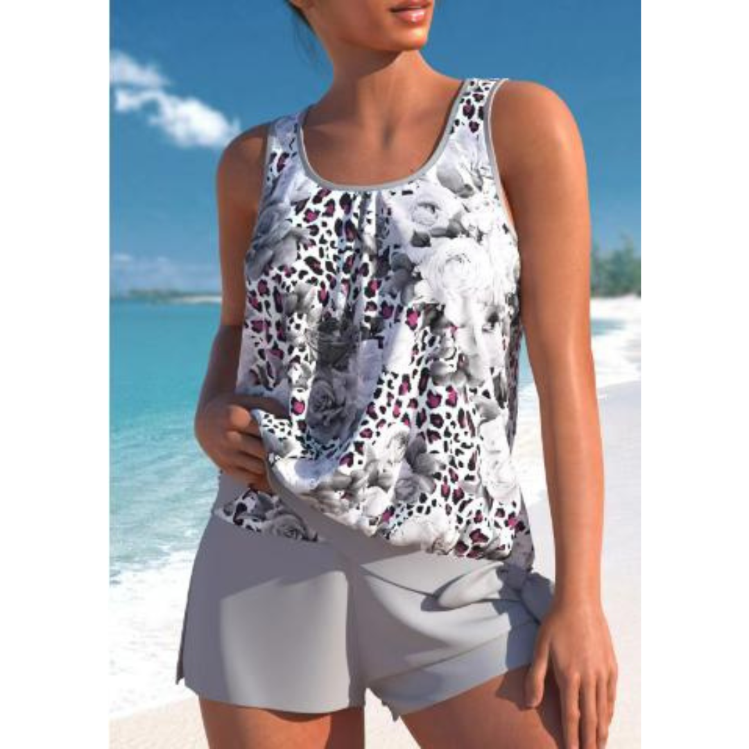 Donna in spiaggia con top floreale bianco e nero e pantaloncini grigi. Moda estiva, abbigliamento casual, look da vacanza al mare.