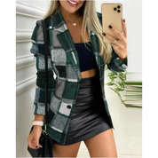 Donna con blazer a quadri verde, top nero e gonna in pelle, scatta selfie con smartphone. Moda autunnale, outfit elegante e casual.