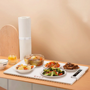 Piatto riscaldante elettrico con cibo vario: stufato, verdure, carne. Design moderno su tavolo da cucina. Accessorio cucina pratico ed elegante.
