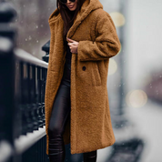 Cappotto lungo in pelliccia sintetica marrone, donna, moda invernale, elegante, caldo, con cappuccio, abbinato a pantaloni neri, strada innevata.
