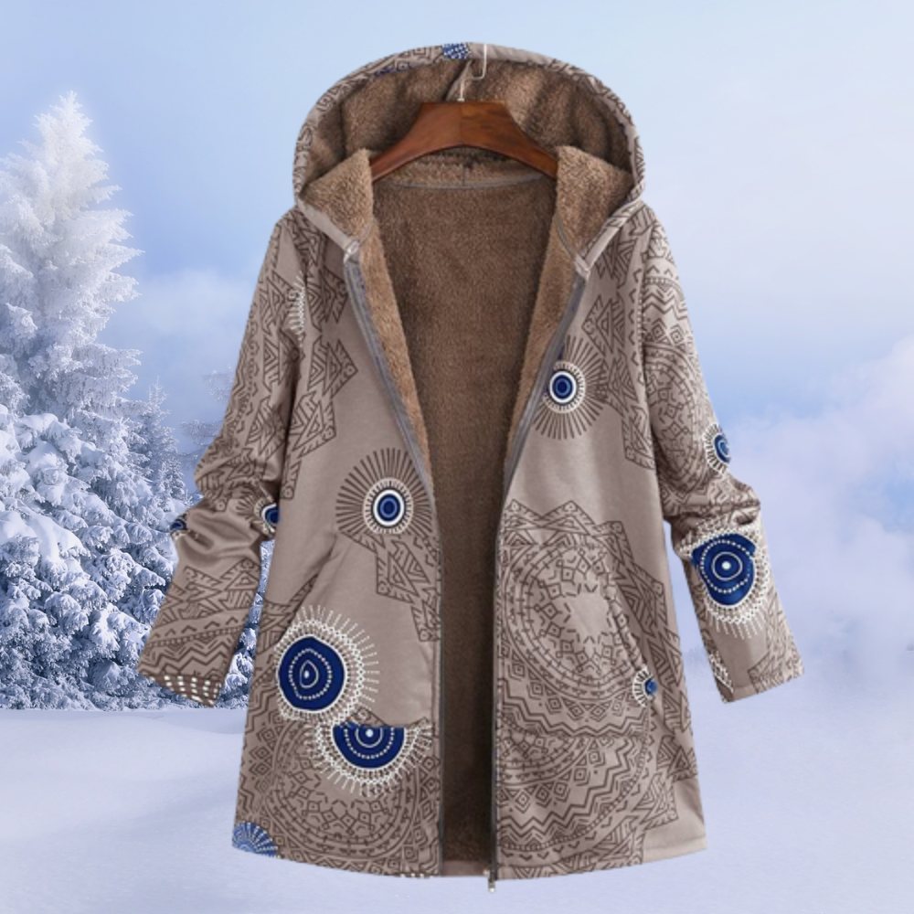 Cappotto invernale con cappuccio, motivo geometrico beige e blu, interno in pelliccia sintetica, appeso su sfondo innevato. Moda donna, abbigliamento caldo.