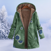 Cappotto invernale verde con cappuccio, motivo geometrico, foderato in pelliccia sintetica, appeso su gruccia, sfondo innevato.