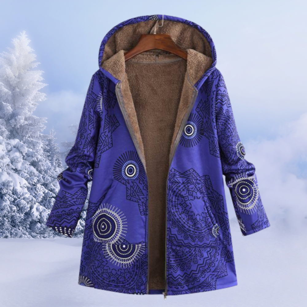 Cappotto invernale con cappuccio, motivo geometrico blu, interno in pelliccia sintetica marrone, appeso su gruccia, sfondo innevato.