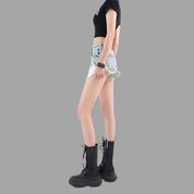 Donna in shorts di jeans strappati, top nero e stivali neri alti. Moda casual estiva, abbigliamento giovanile, stile urbano. Sfondo grigio.