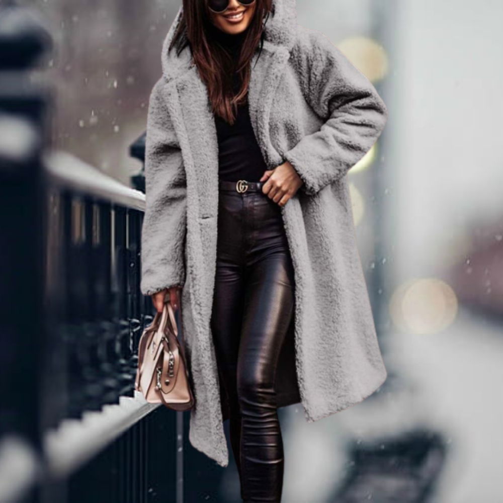 Donna con cappotto in pelliccia sintetica grigia, pantaloni in pelle nera, borsa beige, sorridente in strada innevata. Moda invernale elegante.