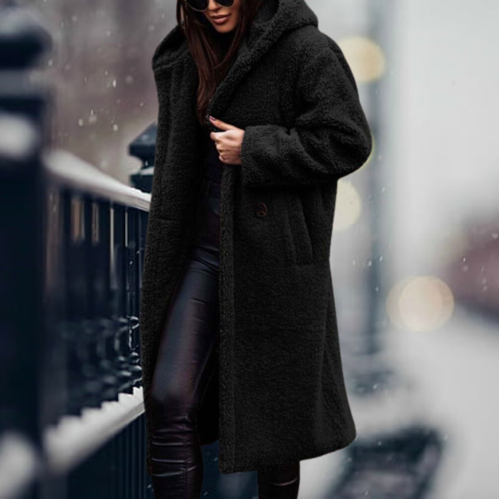 Donna con cappotto nero invernale lungo, tessuto peluche, passeggia in città sotto la neve. Moda invernale, abbigliamento caldo, stile urbano.