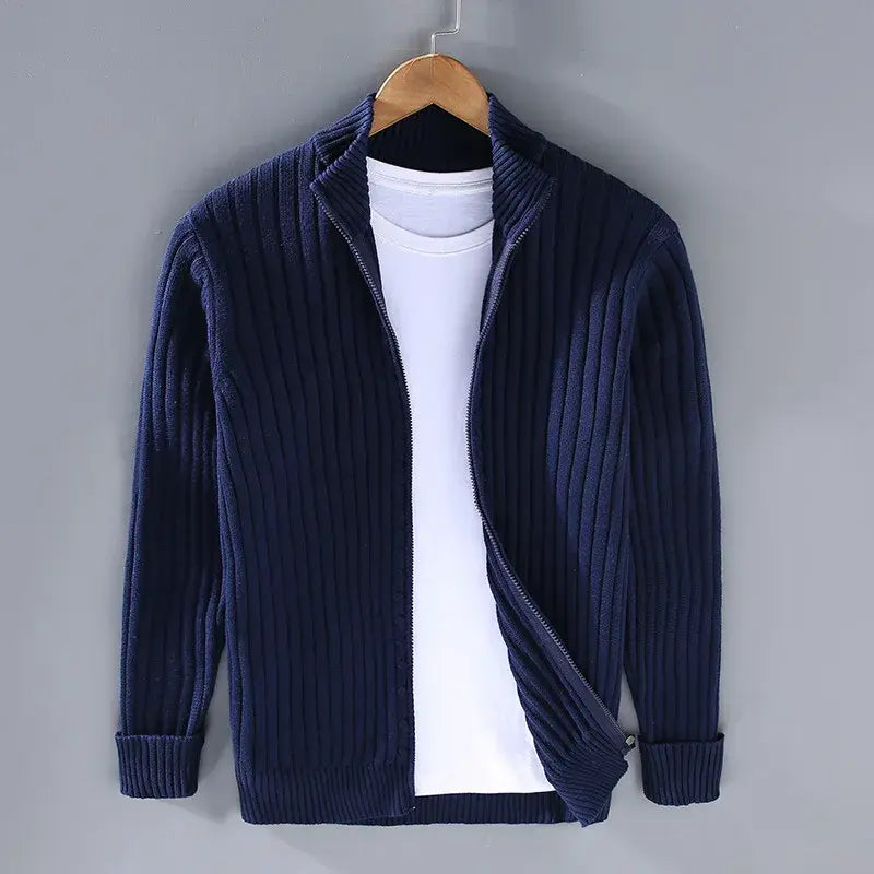 Cardigan blu scuro a coste con zip, appeso su gruccia, sopra maglietta bianca. Moda uomo, abbigliamento casual elegante, tessuto caldo.