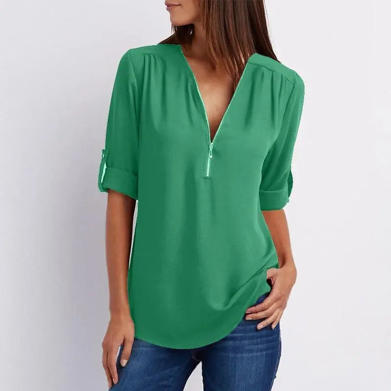 Donna con camicetta verde a maniche lunghe, scollo a V con zip, abbinata a jeans. Moda casual femminile, abbigliamento elegante e confortevole.