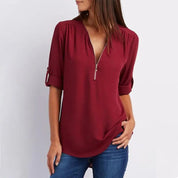 Donna con blusa bordeaux a maniche lunghe, scollo a V con zip, abbinata a jeans. Moda casual femminile, abbigliamento autunnale elegante.