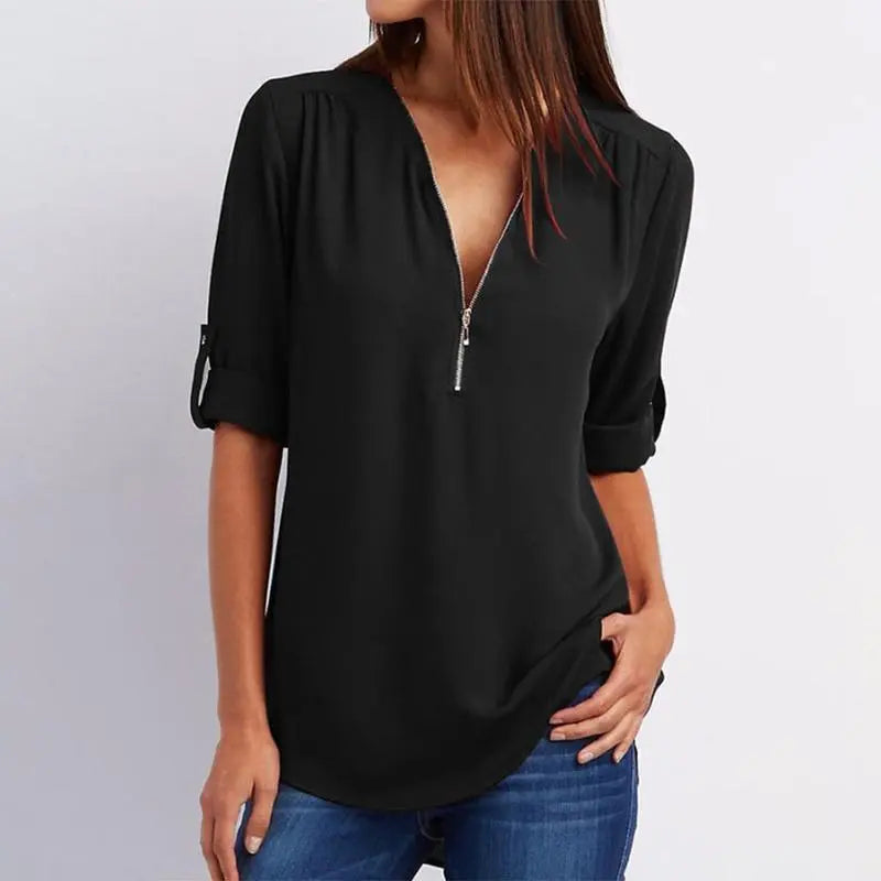 Blusa nera da donna con zip frontale, maniche lunghe arrotolate, scollo a V, abbinata a jeans blu. Moda casual elegante, abbigliamento femminile.