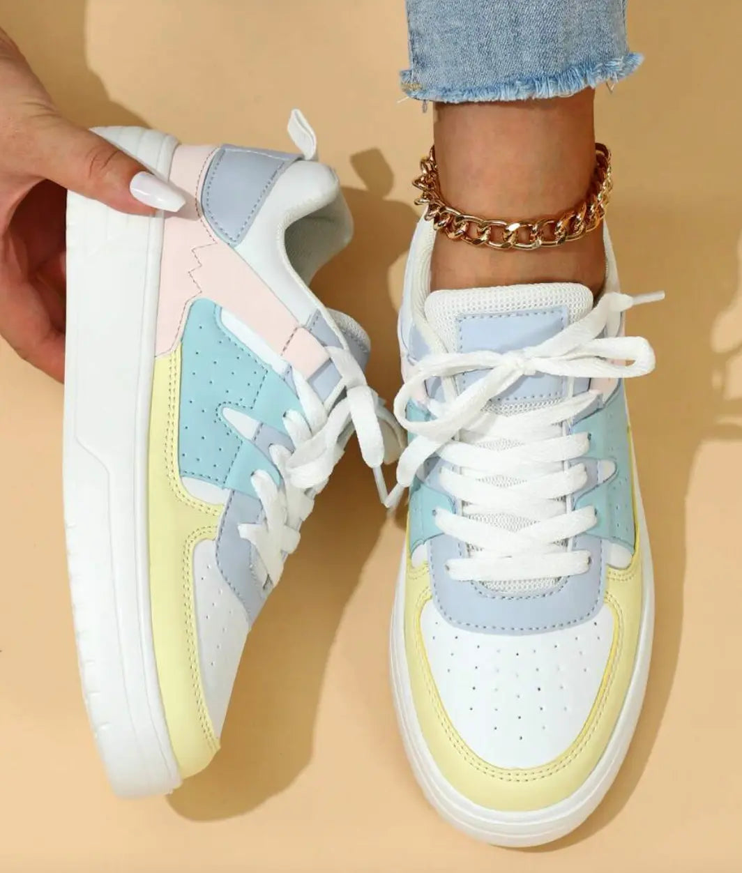Scarpe da ginnastica multicolore pastello per donna, design moderno con lacci bianchi, suola in gomma bianca, indossate con jeans chiari e cavigliera dorata.