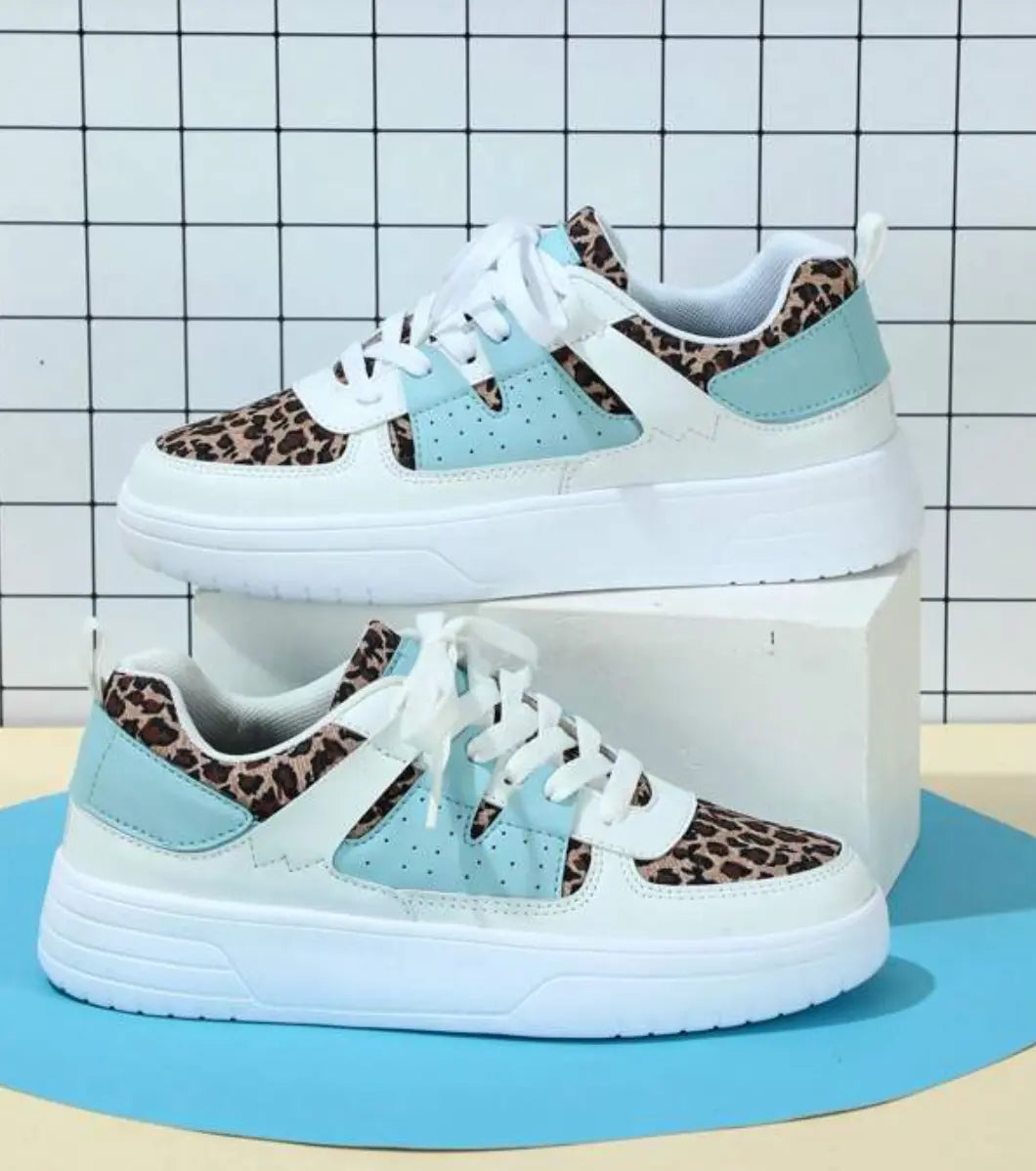 Scarpe da ginnastica bianche con dettagli leopardati e azzurri, su sfondo a griglia. Design moderno, casual e alla moda per uomo e donna.