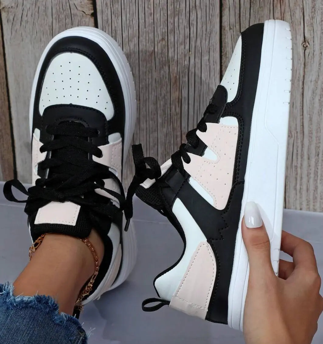 Scarpe da ginnastica bianche e nere con dettagli rosa, su sfondo di legno. Design moderno, suola spessa, perfette per moda casual e sportiva.
