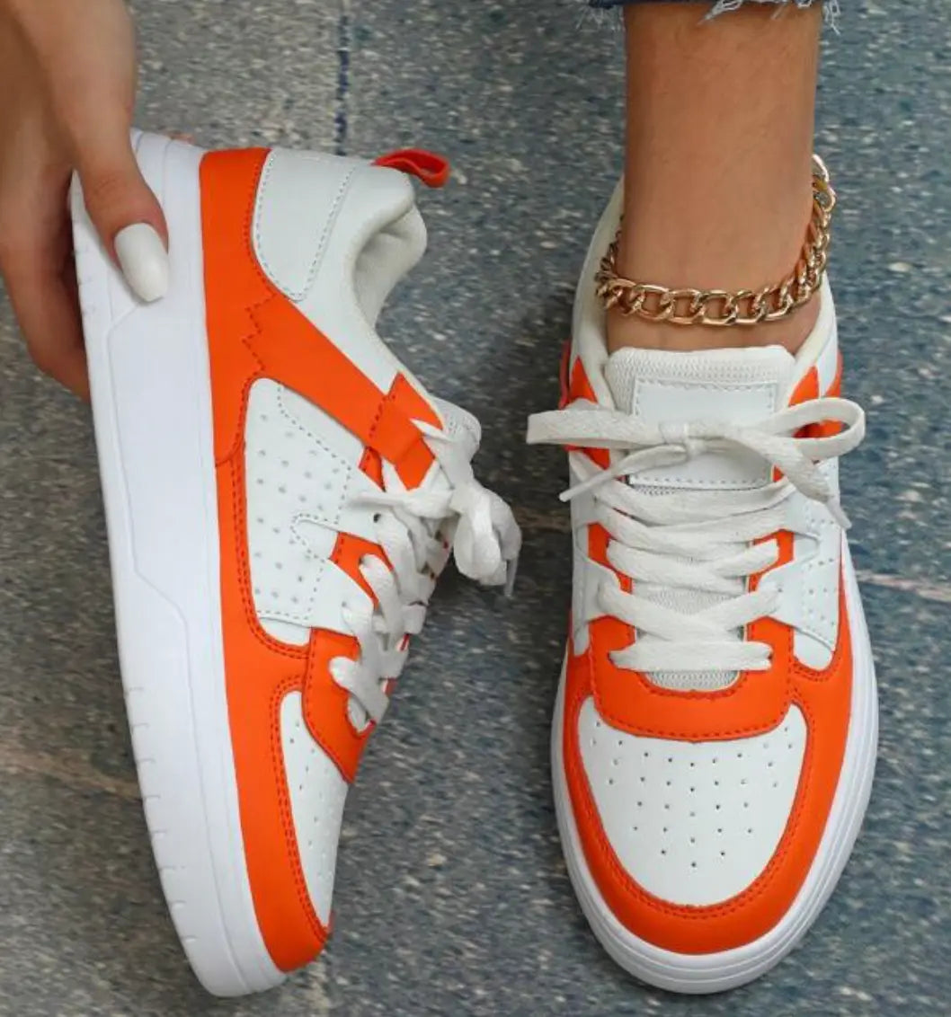 Scarpe da ginnastica bianche e arancioni, design moderno, suola in gomma, lacci bianchi, indossate con cavigliera dorata. Moda casual donna.