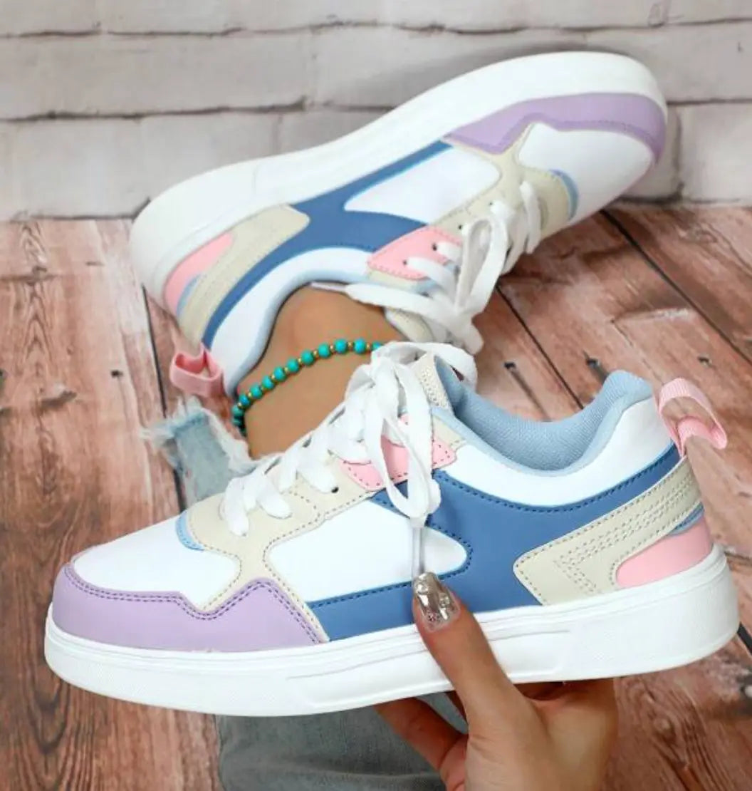 Scarpe da ginnastica multicolore da donna su sfondo in legno, design moderno con dettagli rosa, blu e beige, perfette per look casual e sportivi.