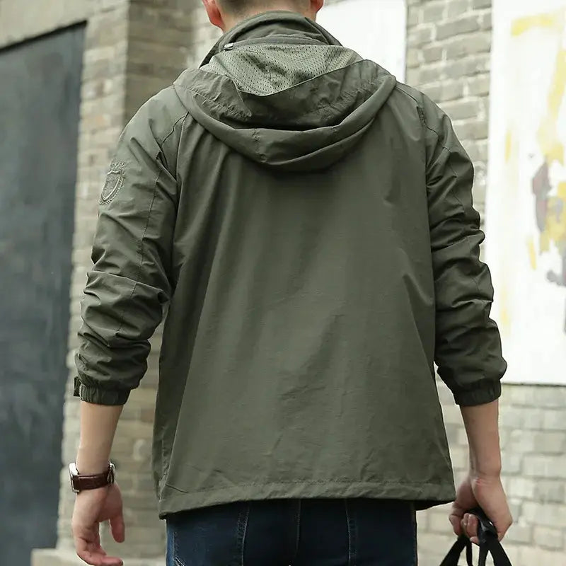 Giacca a vento verde oliva da uomo, vista posteriore, con cappuccio e dettagli ricamati, ideale per moda casual e outdoor.