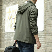 Giacca verde militare uomo, casual, con cappuccio, indossata all'aperto. Moda maschile autunnale, stile urbano, tessuto leggero.