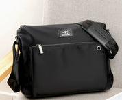 Borsa a tracolla nera in nylon impermeabile, con tasca frontale con zip e tracolla regolabile. Design elegante e pratico per uso quotidiano.