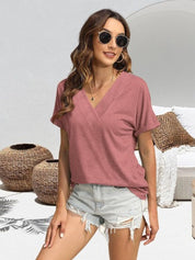 Donna con occhiali da sole indossa maglietta rosa a V e shorts di jeans strappati, sfondo con cesti di vimini e divano bianco. Moda estiva casual.