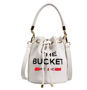 Borsa secchiello bianca in pelle con scritta "The Bucket", manico e tracolla regolabile, dettagli dorati. Elegante e alla moda.