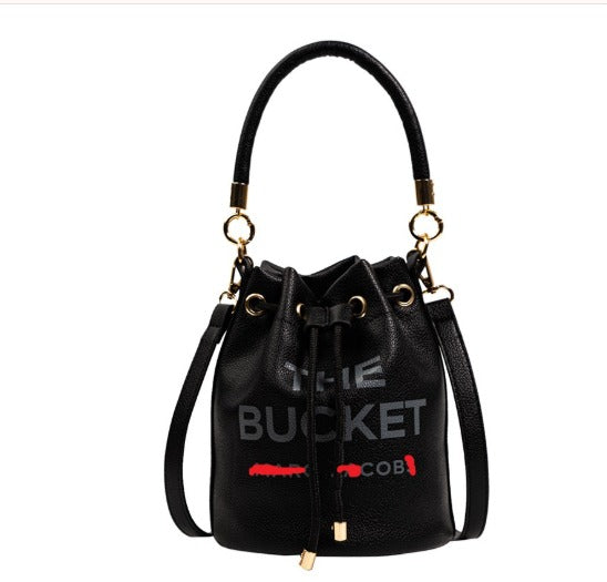 Borsa secchiello nera in pelle con manico e tracolla, dettagli dorati, scritta "The Bucket" e logo rosso. Elegante e moderna, perfetta per ogni occasione.