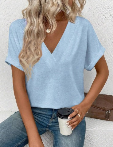 Donna con maglietta azzurra scollo a V, capelli biondi ondulati, jeans, tiene bicchiere di caffè. Moda casual femminile, abbigliamento estivo.