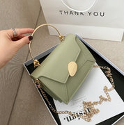 Borsa a tracolla verde salvia con manico dorato e catena, elegante e moderna, su sfondo di scatola regalo e busta "Thank You".