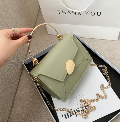 Borsa a tracolla verde salvia con manico dorato e catena, elegante e moderna, su sfondo di scatola regalo e busta "Thank You".