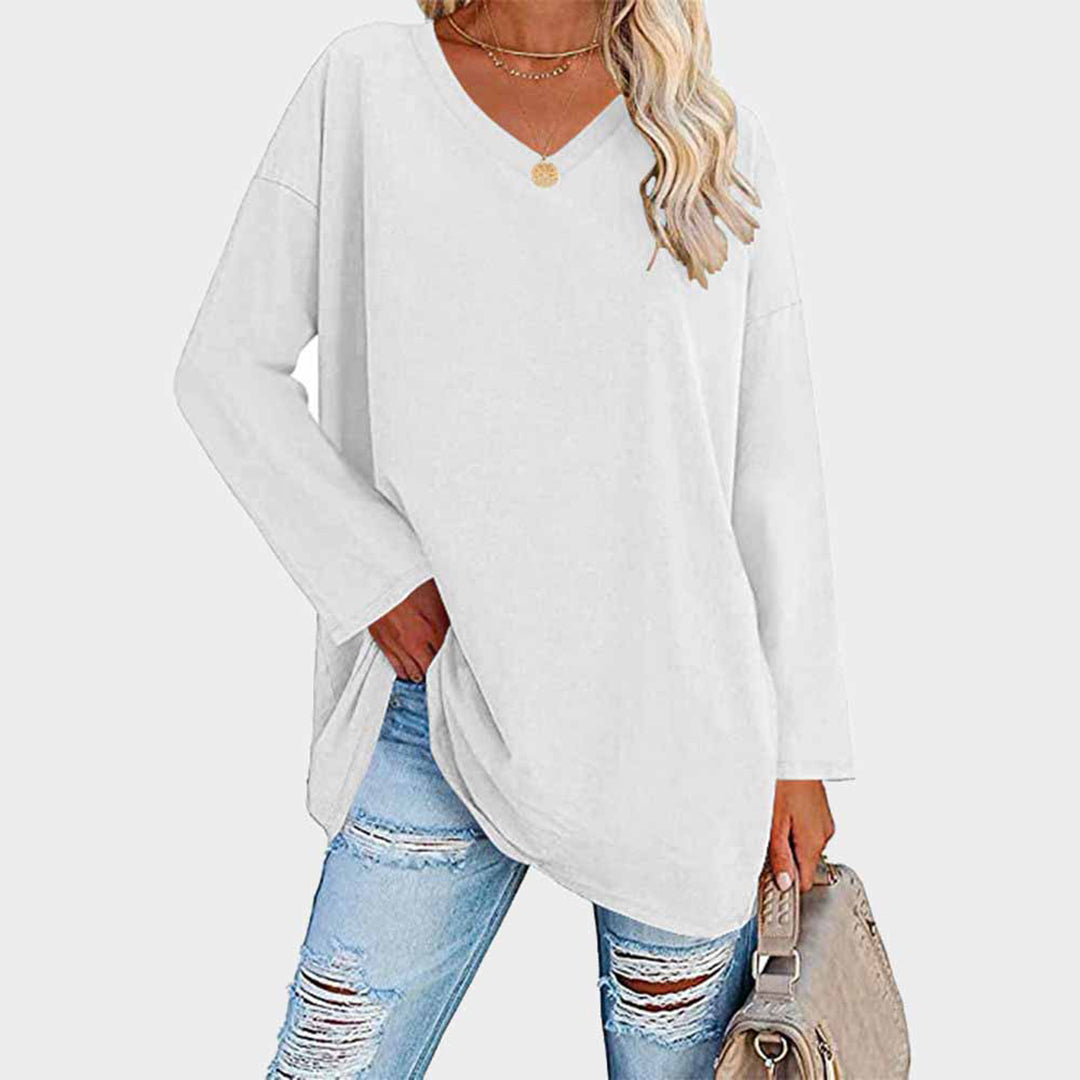 Maglia bianca oversize a maniche lunghe con scollo a V, abbinata a jeans strappati e borsa beige. Moda casual donna, look autunnale.