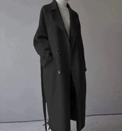 Cappotto lungo nero elegante, doppio petto, con cintura, indossato su maglione bianco. Moda autunnale, abbigliamento donna, stile minimalista.