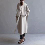 Cappotto lungo beige donna, design elegante, cintura in vita, abbinato a pantaloni neri e tacchi alti. Moda autunnale, stile minimalista.
