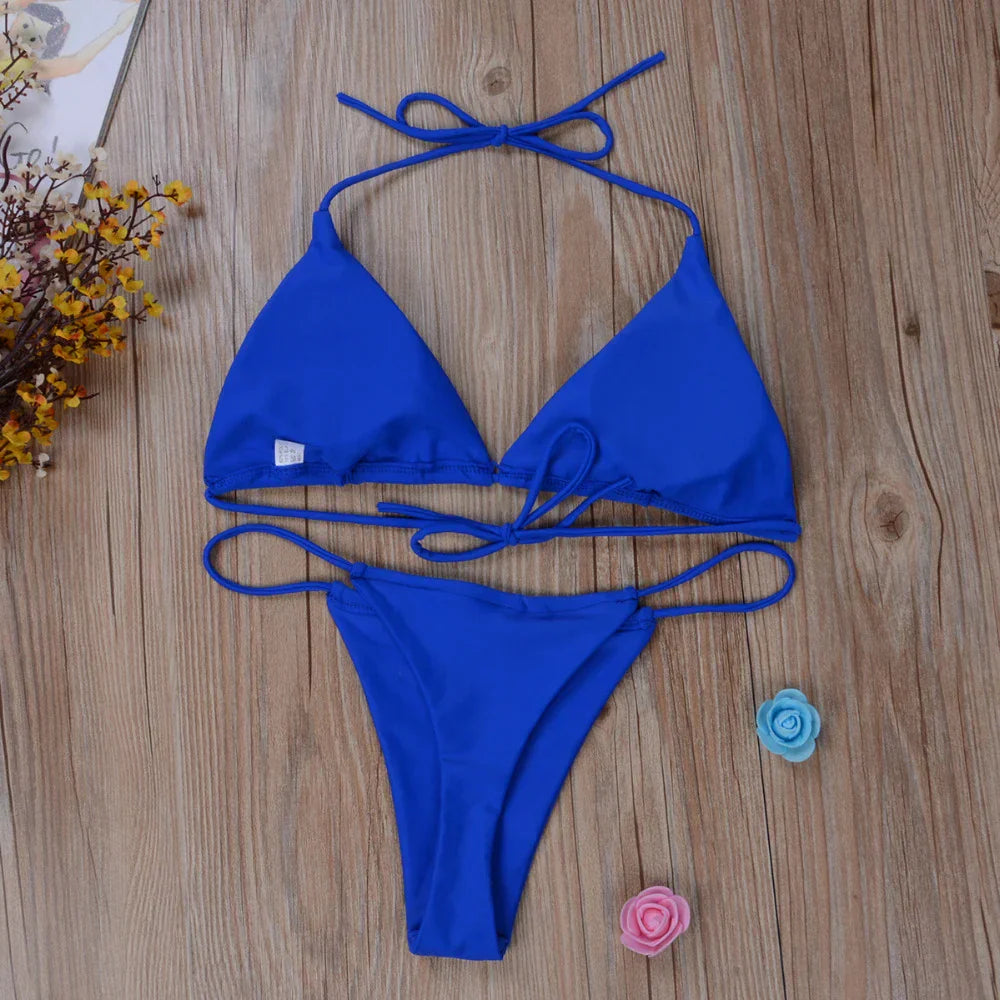 Bikini blu a triangolo su pavimento in legno, con fiori decorativi. Costume da bagno estivo, moda mare donna, stile elegante e moderno.