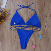 Bikini blu a triangolo su pavimento in legno, con fiori decorativi. Costume da bagno estivo, moda mare donna, stile elegante e moderno.