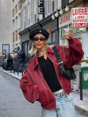 Donna con giacca rossa oversize, berretto nero e occhiali da sole, posa in strada urbana. Moda street style, look casual chic, tendenze autunno.