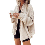 Donna con cardigan beige oversize e pantaloncini neri, tiene una tazza bianca. Moda casual autunnale, abbigliamento comodo e trendy.
