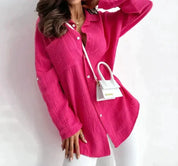 Donna con camicia oversize rosa acceso, borsa a tracolla bianca, pantaloni bianchi. Moda femminile, abbigliamento casual elegante.