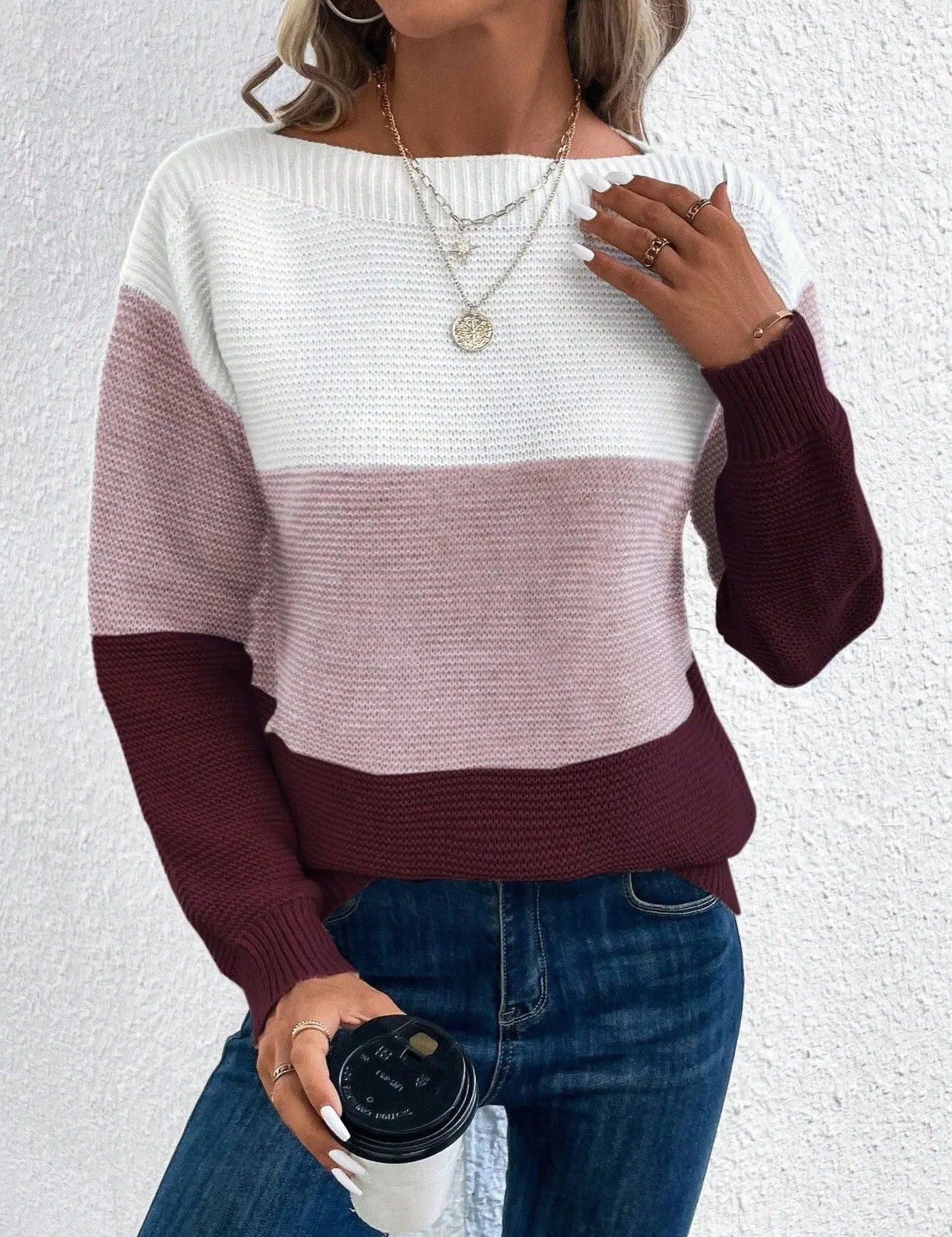 Maglione donna a righe bianche, rosa e bordeaux, indossato con jeans. Accessori: collane dorate, anelli, caffè da asporto. Moda casual autunnale.