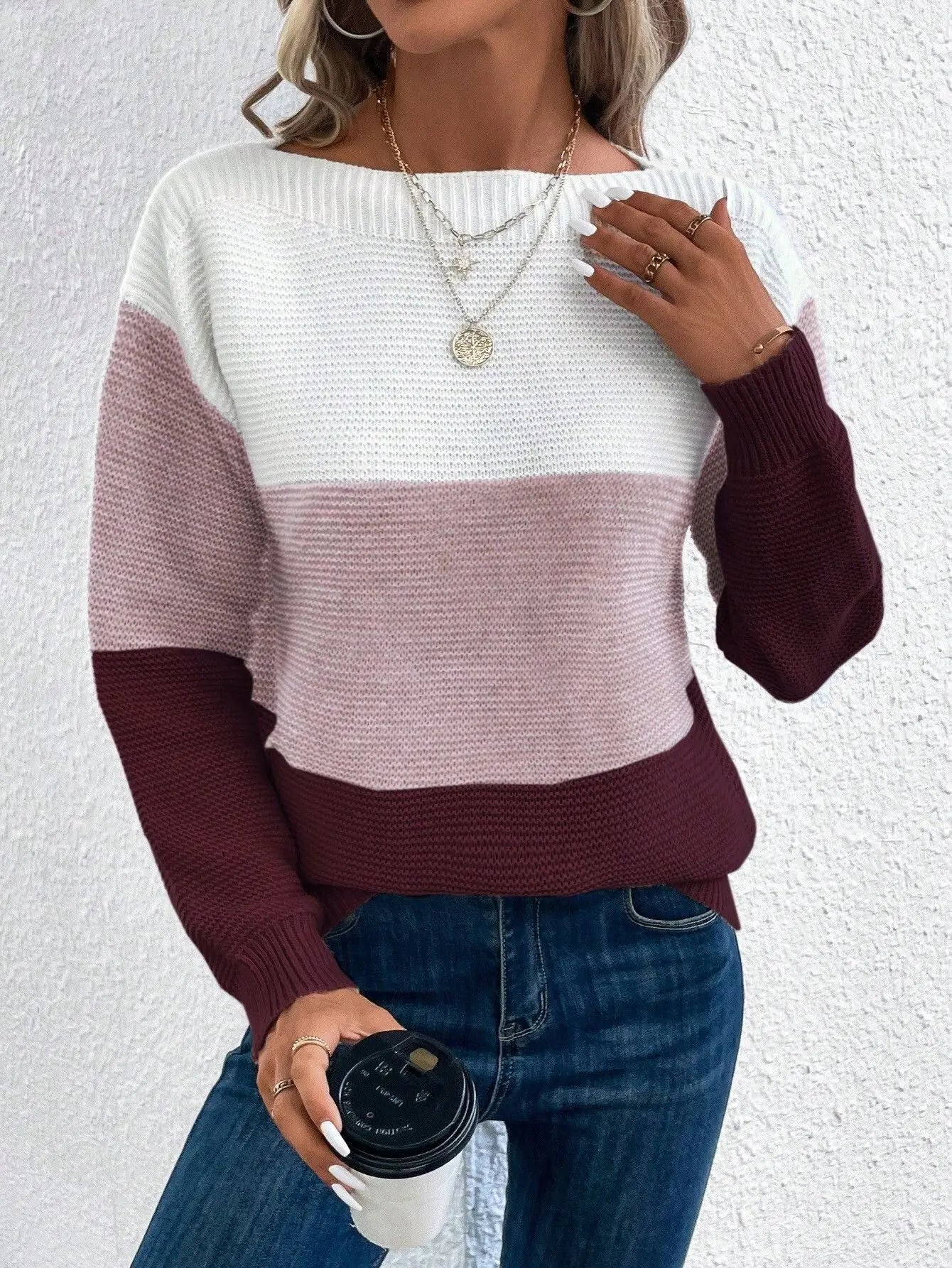 Maglione donna a righe bianche, rosa e bordeaux, indossato con jeans. Accessori: collane dorate, anelli, caffè da asporto. Moda casual autunnale.