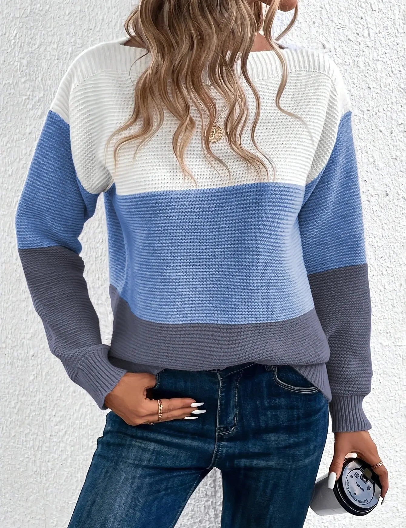 Maglione a righe blu, bianco e grigio, donna di spalle, capelli ondulati, jeans blu, sfondo bianco. Moda casual autunnale, stile moderno.