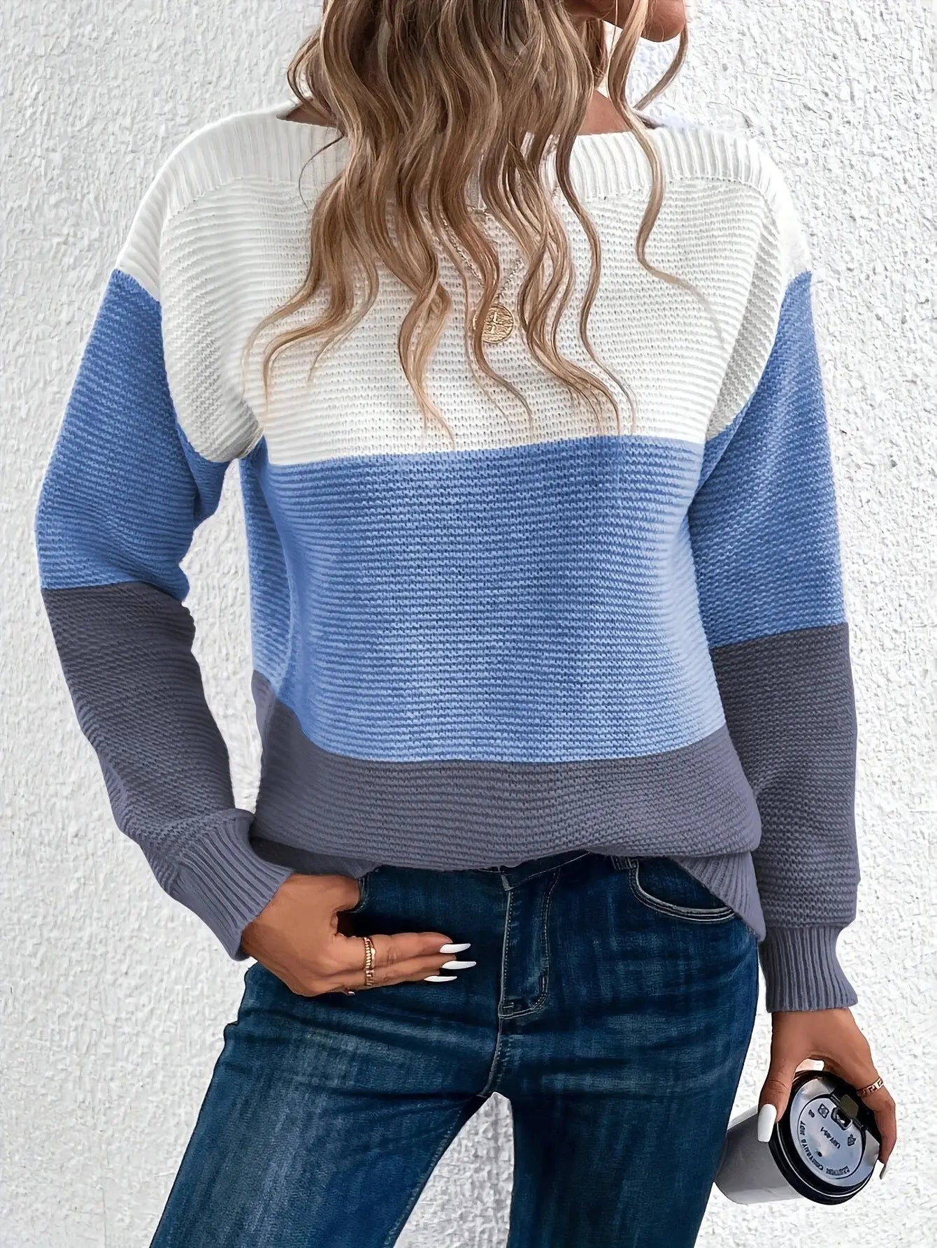 Maglione a righe blu, bianco e grigio, donna di spalle, capelli ondulati, jeans blu, sfondo bianco. Moda casual autunnale, stile moderno.