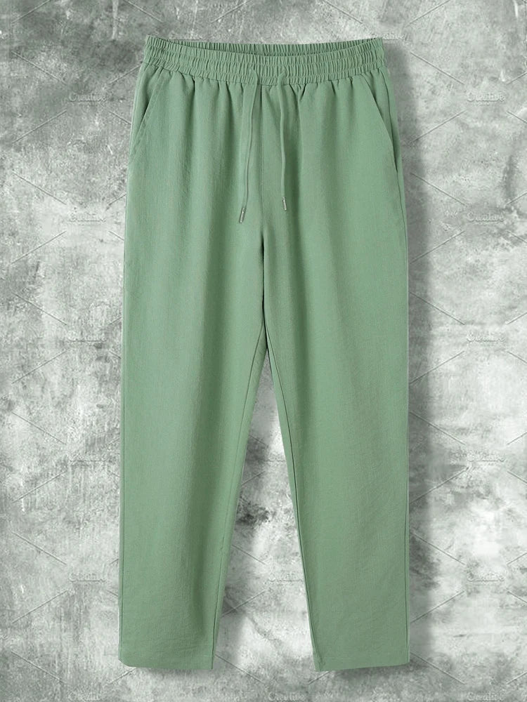 Pantaloni verdi da uomo in cotone, design casual con elastico in vita e coulisse, su sfondo grigio. Ideali per moda estiva e comfort quotidiano.