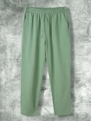Pantaloni verdi da uomo in cotone, design casual con elastico in vita e coulisse, su sfondo grigio. Ideali per moda estiva e comfort quotidiano.