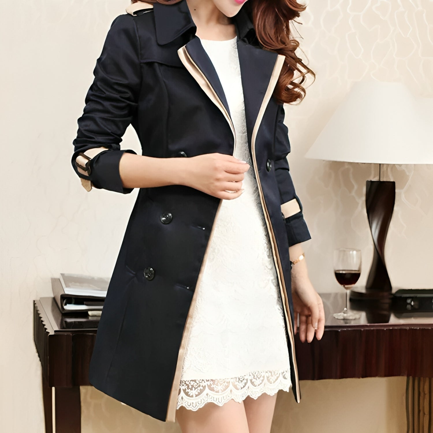 Cappotto trench nero elegante da donna su abito bianco in pizzo, moda autunnale, stile classico, sfondo interno con lampada e bicchiere di vino.