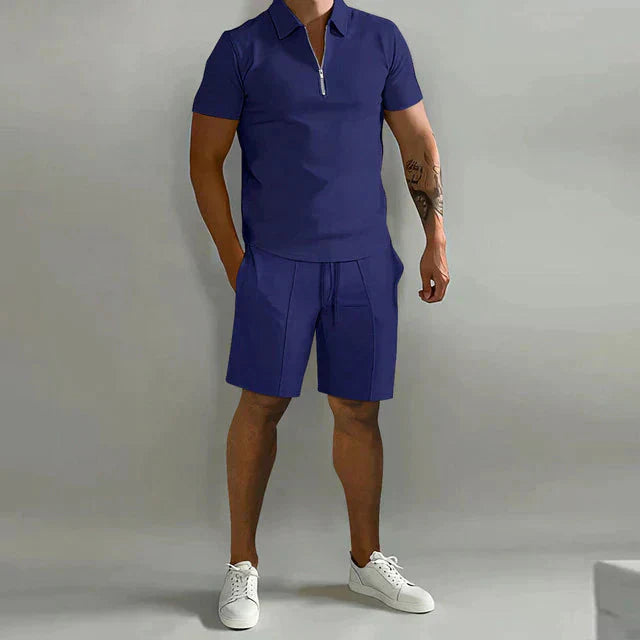 Abbigliamento uomo estivo: completo casual blu con polo a zip e pantaloncini, scarpe bianche. Stile moderno e confortevole.