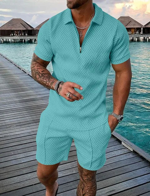 Uomo in completo estivo azzurro su passerella di legno, sfondo mare e bungalow. Moda maschile, abbigliamento casual, vacanza tropicale.