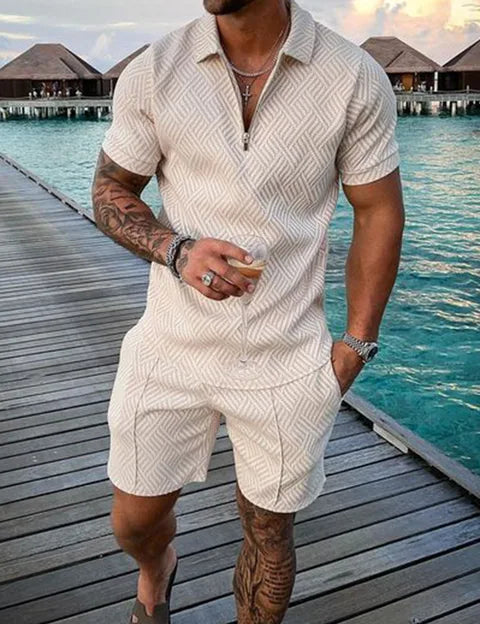 Uomo in completo estivo beige con motivo geometrico, su passerella di legno vicino al mare. Moda maschile, abbigliamento casual estivo.