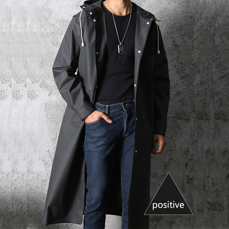 Cappotto impermeabile nero da uomo, lungo, con cappuccio, indossato su maglia nera e jeans. Stile casual, moda autunnale.