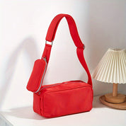 Borsa a tracolla rossa con tasca con zip, design moderno, su tavolo bianco accanto a lampada da tavolo. Accessorio moda donna elegante.