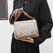 Borsa a tracolla beige con motivo monogramma, dettagli in pelle marrone e chiusure a zip, indossata da una persona in abito nero.